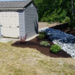 exterior photo of shrubs planted in landscaping next to stone drainage system